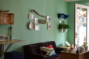 Sofa und Tisch vor grünlicher Wand, links ein Stehtisch, rechts offene Glastür mit Spiegelung